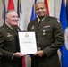 Two U.S. Army officers in olive green dress uniforms are posing together while holding a Certificate of Retirement. The certificate is issued to Brigadier General Theodore Roosevelt Scott III upon his retirement from the United States Army. The ceremony appears to be a formal military retirement event with flags displayed in the background.