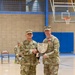 Two U.S. Army soldiers in OCP (Operational Camouflage Pattern) uniforms are posing together in a gymnasium while jointly holding a shield-shaped plaque or award. The soldier on the left, identified by his name tape as 'CLEGHORN,' appears to hold a general officer rank insignia on his cap. The soldier on the right is wearing a medal on his chest, suggesting this is an awards or recognition ceremony.