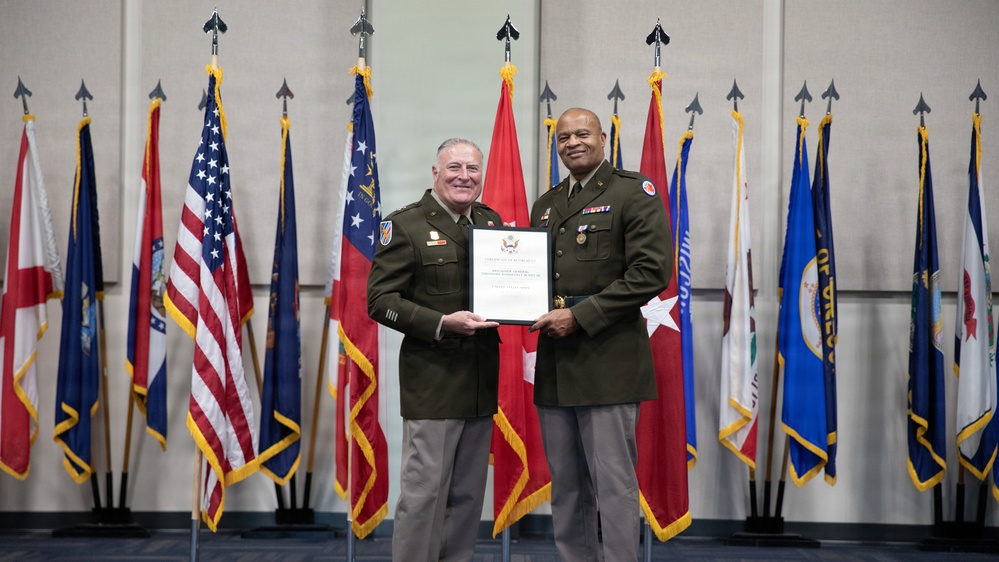Two U.S. Army officers in olive green service uniforms are posing together while jointly holding an official certificate or commendation document. The ceremony appears to be a formal military award or recognition presentation, taking place in front of an array of U.S. state and military flags. Both individuals are smiling, suggesting a positive ceremonial occasion.