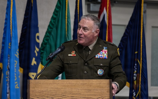 A senior military officer in U.S. Army dress greens uniform is speaking at a podium bearing the Georgia National Guard seal. The setting appears to be an official military ceremony or briefing, with multiple flags displayed in the background. The officer is wearing numerous medals, ribbons, and insignia indicating high rank and extensive service.