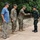 U.S. Marines and Thailand Mine Action Center participate in Deployed for Training Bilateral EOD Exercise The image shows a meeting between military personnel on a paved outdoor path surrounded by trees. Two individuals in US Marine Corps MARPAT camouflage uniforms are present, one of whom is shaking hands with a person in a different camouflage uniform, likely Thai military based on the distinctive pattern and black cap with insignia. A civilian in a blue t-shirt and cap stands nearby observing the interaction.