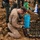 U.S. Marines and Thailand Mine Action Center participate in Deployed for Training Bilateral EOD Exercise The image shows what appears to be an explosive ordnance disposal (EOD) operation, likely in Southeast Asia based on the Thai military uniforms visible. A specialist in tan/khaki coveralls is kneeling over a large cache of unearthed munitions, including what appear to be mortar rounds, landmines, and other ordnance laid out in rows. Military personnel in camouflage uniforms are working in the background at an excavation site.