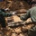 U.S. Marines and Thailand Mine Action Center participate in Deployed for Training Bilateral EOD Exercise Two personnel in military/tactical clothing are handling a large collection of corroded, cylindrical munitions or ordnance items that have been excavated from the ground. The items appear to be old, heavily rusted artillery shells or similar explosive ordnance arranged in rows on disturbed soil. This appears to be an unexploded ordnance (UXO) clearance or explosive ordnance disposal (EOD) operation.
