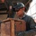 U.S. Marines and Thailand Mine Action Center participate in Deployed for Training Bilateral EOD Exercise A military personnel wearing olive green uniform, boonie hat, and sunglasses is handling a wooden crate near what appears to be a military vehicle or truck. The individual has visible patches on their uniform sleeve, including what appears to be a flag patch. At least one other uniformed person is visible in the background.