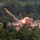 U.S. Marines and Thailand Mine Action Center participate in Deployed for Training Bilateral EOD Exercise The image captures a large explosion with an orange fireball and smoke cloud occurring in an open sandy area surrounded by dense tropical forest. Bright projectile trails with sparks are visible arcing upward and outward from the blast point. Colored marker flags are visible in the field, suggesting a controlled or designated detonation zone.
