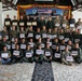 A large group of military personnel from Thailand and the United States pose together for a group photo holding certificates at what appears to be a bilateral training exercise completion ceremony. The backdrop displays a banner reading 'DEPLOY FOR TRAINING BILATERAL EOD EXERCISE' along with Thai and American flags and unit insignia. Participants are arranged in multiple rows under an open-air pavilion.