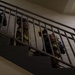 Multiple firefighters in full turnout gear are ascending an interior stairwell, viewed from a low angle looking upward. They are equipped with SCBA (Self-Contained Breathing Apparatus) tanks and wearing standard firefighting protective clothing with yellow reflective striping. The scene appears to depict a training exercise or active emergency response inside a building.