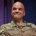 A U.S. Army soldier wearing an OCP (Operational Camouflage Pattern) uniform is smiling and looking upward to his right. The name tape on his uniform reads 'RANNEY' and the branch tape reads 'U.S. ARMY.' He appears to be in an indoor setting with a colorful background.