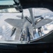This image is taken from the boom operator's station of a tanker aircraft, showing an aerial refueling operation in progress. A fighter jet, identifiable as an F-15 Eagle, is positioned directly below the refueling boom, receiving fuel at altitude above a cloud layer. The markings 'ARS' and the number '909' are visible on the tanker's wing or fuselage.