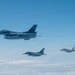 Three military jet fighters are flying in a loose formation at altitude above a cloud layer against a clear blue sky. The formation consists of two single-engine fighters that appear to be F-2 or F-16 variants in the foreground and middle, and a twin-engine fighter that appears to be an F-15 variant on the right. The aircraft display markings consistent with the Japan Air Self-Defense Force (JASDF).