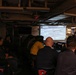 A group of military personnel are attending a briefing or training session in what appears to be a shipboard compartment. They are seated facing a projected presentation screen displaying a 'Radian Rule Reference' slide, which contains navigational or tactical formulas and diagrams. The setting, chair markings, and uniforms suggest a U.S. Navy vessel.