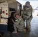 Three U.S. Army Military Police soldiers are performing maintenance on a HMMWV (Humvee) vehicle, specifically working on the front tire. The vehicle is marked '603 MP CO TRK 006', identifying it as belonging to the 603rd Military Police Company. The scene takes place in what appears to be a motor pool or maintenance bay.