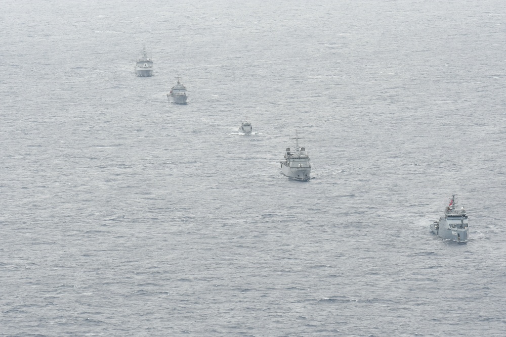 An aerial photograph shows five naval vessels sailing in a loose diagonal formation across open ocean. The ships appear to be gray-painted military vessels of varying sizes, likely conducting a joint naval exercise or patrol operation. The image is taken from altitude under overcast conditions, giving the scene a muted, hazy appearance.