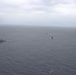 An aerial photograph showing a formation of multiple naval vessels underway on an overcast, grey sea. At least five ships are visible spread across the frame, suggesting a multi-ship naval exercise or transit operation. Visibility is reduced due to hazy, overcast weather conditions.