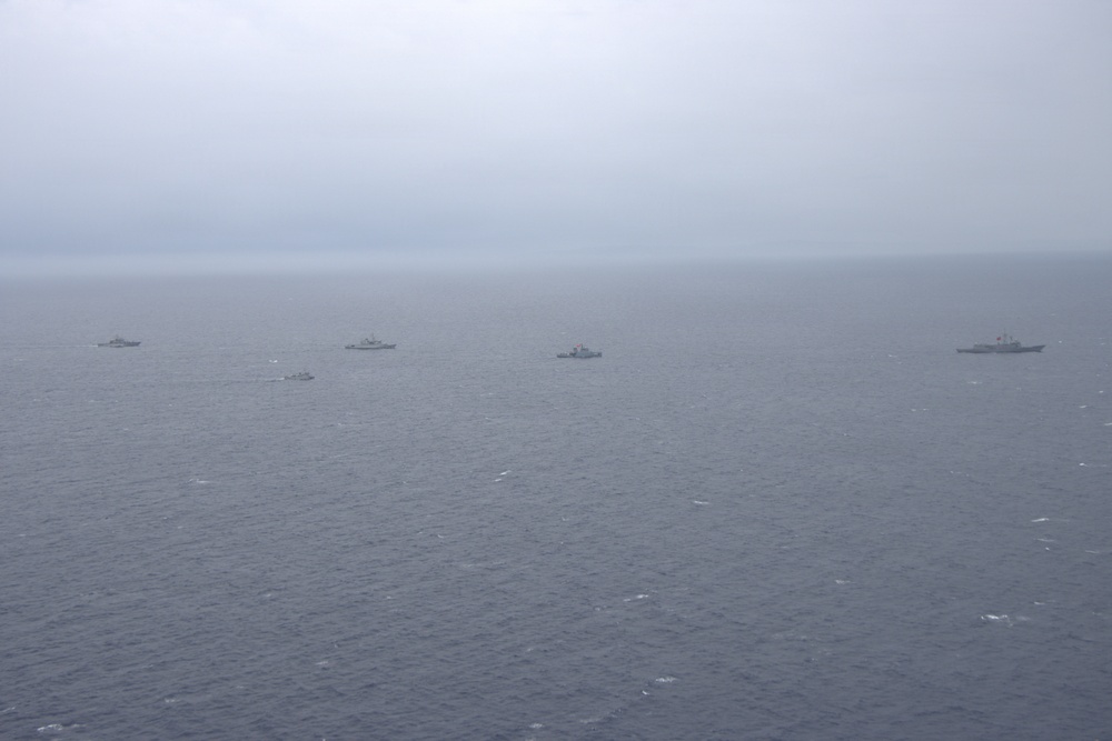 An aerial or elevated photograph showing a formation of approximately six naval vessels spread across an open ocean under overcast, hazy conditions. The ships appear to be operating in a loose formation, possibly during a naval exercise or patrol. Weather conditions are poor with low visibility and a grey, cloud-covered sky.