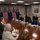 A formal bilateral meeting between United States and Australian officials is taking place in what appears to be a government conference room, likely the Pentagon or a similar high-level facility. Participants are seated around a large oval conference table with both American and Australian flags displayed prominently in the background. The setting suggests a high-level diplomatic or defense meeting between the two allied nations.