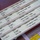 The image shows a set of aviation flight progress strips used in air traffic control, arranged in a strip holder on a desk. Each strip contains coded flight information including aircraft identifiers, altitudes, routes, and waypoints. A reference document for Hi-Alt Routes is partially visible beneath the strips.