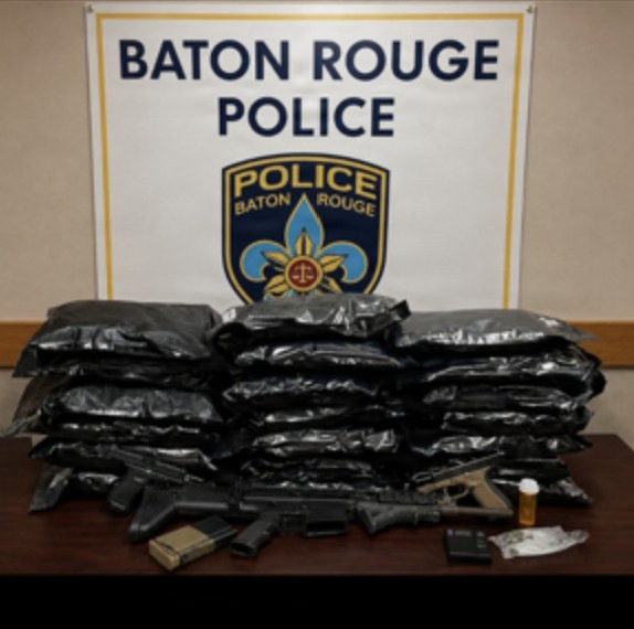 This is an official law enforcement evidence display photograph from the Baton Rouge Police Department. The image shows seized contraband, weapons, and related items arranged on a table in front of an official BRPD sign and badge logo. This appears to be a standard press/evidence documentation photo used by law enforcement agencies.
