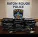 This is an official law enforcement evidence display photograph from the Baton Rouge Police Department. The image shows seized contraband, weapons, and related items arranged on a table in front of an official BRPD sign and badge logo. This appears to be a standard press/evidence documentation photo used by law enforcement agencies.