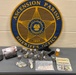 This is an evidence display photograph taken by the Ascension Parish Sheriff's Office in Louisiana. The image shows seized contraband and related items laid out on a table in front of the official agency seal. This appears to be a standard law enforcement evidence documentation photograph.