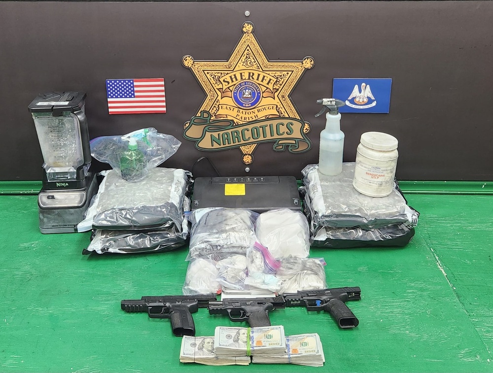 This is an official law enforcement evidence display photograph from the East Baton Rouge Parish Sheriff's Office Narcotics Division. The image shows seized contraband, weapons, currency, and drug paraphernalia arranged in front of the agency's official insignia. This type of photograph is standard procedure for documenting narcotics seizures.