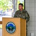 A U.S. Air Force officer, wearing OCP (Operational Camouflage Pattern) uniform with a two-star Major General rank insignia, is speaking at a podium bearing the Vermont National Guard seal. The seal displays the motto 'Freedom &amp; Unity' and the year 1770. The setting appears to be an indoor/covered outdoor venue with natural light visible through windows in the background.