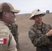 A U.S. Marine (identified by name tape 'HUYNH' and MARPAT camouflage uniform) is demonstrating or explaining a pistol to a Peruvian military personnel (identified by the Peruvian flag patch on the left shoulder). The interaction appears to take place on a sandy outdoor firing range or training area. This appears to be a joint military training or exchange exercise between U.S. Marines and Peruvian armed forces.