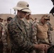 A group of military personnel from at least two different nations are gathered at what appears to be an outdoor firing range or training area in a desert environment. A U.S. Marine in MARPAT camouflage and a pith helmet is handling a pistol, likely during a weapons familiarization or training exercise. Several soldiers wearing Peruvian flag patches on their uniforms are observing, suggesting a joint military training exercise.