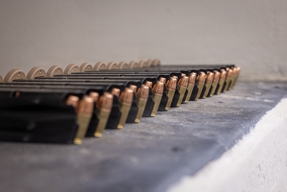 The image shows multiple loaded firearm magazines arranged in a row on a flat surface, likely a shooting range bench or table. Each magazine is loaded with what appear to be jacketed hollow point (JHP) or full metal jacket (FMJ) pistol cartridges with copper-colored projectiles and brass casings. The magazines are black polymer or metal and are lined up in a uniform, organized manner.