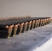 The image shows multiple loaded firearm magazines arranged in a row on a flat surface, likely a shooting range bench or table. Each magazine is loaded with what appear to be jacketed hollow point (JHP) or full metal jacket (FMJ) pistol cartridges with copper-colored projectiles and brass casings. The magazines are black polymer or metal and are lined up in a uniform, organized manner.