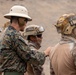 The image shows military personnel engaged in what appears to be a training or briefing exercise in an arid, desert-like environment. At least two soldiers wear helmets marked 'Infanteria de Marina' (Marine Infantry) with Peruvian flag patches, while one individual in green digital camouflage and a pith helmet appears to be instructing or inspecting them. The setting and insignia suggest a joint military exercise involving Peruvian Marine Infantry.