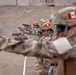 A line of military personnel in desert camouflage uniforms are conducting a pistol shooting exercise at an outdoor firing range. The soldiers are wearing tactical helmets bearing what appears to be the Peruvian flag patch, along with eye and ear protection. The setting is an arid, sandy environment consistent with a military training facility.