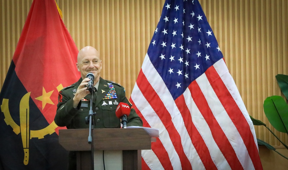 A senior U.S. Army general officer is speaking at a podium during an official press conference or diplomatic event. He is flanked by the American flag and what appears to be the Angolan flag, suggesting a bilateral military or diplomatic engagement. A microphone labeled 'TPA' (Televisão Pública de Angola) is visible at the podium.