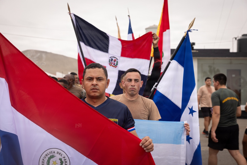 A group of men in military or athletic attire are gathered outdoors holding multiple Latin American national flags. The foreground prominently features the flags of Paraguay and Honduras, with the Dominican Republic flag visible in the background along with other unidentified flags. The setting appears to be a military base or training facility, suggesting a multinational military exercise or ceremony.