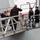 The image shows a formal naval boarding or arrival ceremony on the gangway of a warship. Several personnel in naval dress uniforms are rendering salutes, while others in military camouflage and civilian attire are also present on the gangplank. The scene appears to depict an official visit or dignitary arrival at a naval vessel.