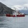 A Canadian Coast Guard vessel named 'CCGS George R. Pearkes' is navigating calm arctic or subarctic waters surrounded by dramatic rocky mountains and overcast skies. The ship displays the distinctive red hull and white superstructure with Canadian maple leaf livery typical of Canadian Coast Guard icebreakers. The scene appears to be in a fjord-like environment, possibly in northern Canada or Greenland.