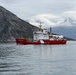A Canadian Coast Guard vessel named 'CCGS George R. Pearkes' is navigating calm arctic or subarctic waters surrounded by dramatic rocky mountains and overcast skies. The ship displays the distinctive red hull and white superstructure with Canadian maple leaf livery typical of Canadian Coast Guard icebreakers. The scene appears to be in a fjord-like environment, possibly in northern Canada or Greenland.