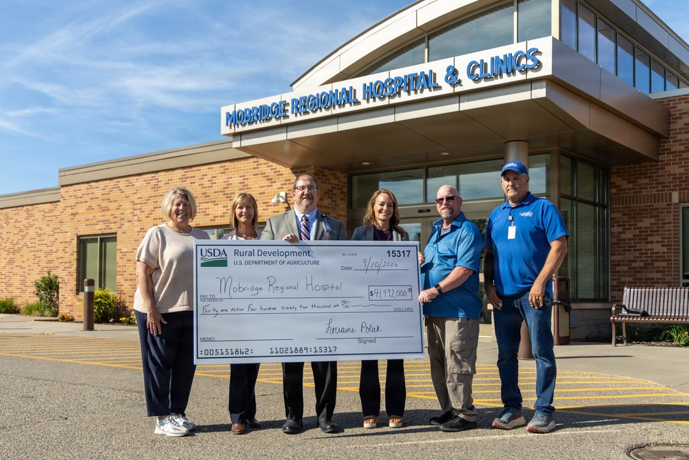Six individuals are posing in front of Mobridge Regional Hospital &amp; Clinics holding a large ceremonial check from USDA Rural Development made out to Mobridge Regional Hospital for $41,492,000, dated 9/10/2026. The check is signed by Lorraine Polak and bears check number 15317. This appears to be a grant or loan award presentation ceremony.