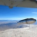 An air-launched missile or munition is captured in the moment of release from the underside of a military aircraft, photographed from a chase camera or onboard camera on the carrying aircraft. The weapon is falling away over an arid desert landscape, likely a test range environment based on the terrain features. The clear blue sky and high altitude suggest this is a controlled test or demonstration event.