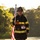 Audubon Park Hosts the 2026 New Orleans 9/11 Heroes Run A firefighter in full turnout gear carries an American flag while participating in what appears to be a 9/11 Heroes Run event. The individual wears a black helmet marked '360' and 'Fire Dept' and displays race bib number 170. The image is taken outdoors during early morning or late afternoon light with trees visible in the background.