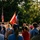 Audubon Park Hosts the 2026 New Orleans 9/11 Heroes Run A military color guard ceremony is taking place outdoors, likely at a patriotic or memorial event. Uniformed personnel are carrying multiple flags including the American flag and what appears to be a U.S. Marine Corps flag, while a crowd of civilians watches. The scene is bathed in warm golden-hour sunlight with lush green trees in the background.