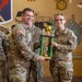 Two U.S. Army soldiers in OCP (Operational Camouflage Pattern) uniforms are jointly holding a trophy during what appears to be an award ceremony. The trophy plaque reads '2026 Tactical Senior Chef of the Year I Corps,' indicating a culinary excellence recognition. The ceremony is taking place indoors in front of a painted mural featuring military insignia and imagery.