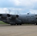 A U.S. Air Force C-130 Hercules military transport aircraft is taxiing on a concrete runway apron with all four turboprop engines running, as evidenced by the spinning propeller blur. The aircraft bears tail number 23023 and is assigned to the 910th Airlift Wing (910 AW) of the Air Force Reserve Command (AFRC). The image was taken in good lighting conditions with a partly cloudy sky and green treeline visible in the background.