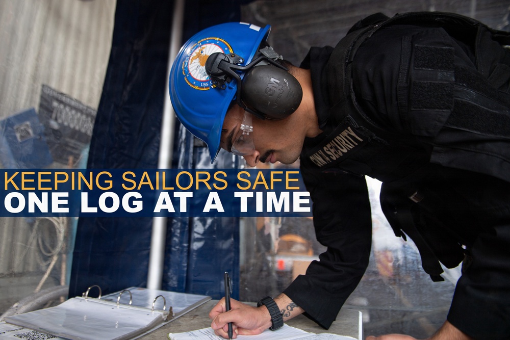 A U.S. Navy security personnel member is writing in a logbook at what appears to be a checkpoint or watch station. The individual is wearing a blue Navy hard hat with an official seal, hearing protection, safety glasses, and a black tactical security vest. An overlay text reads 'KEEPING SAILORS SAFE ONE LOG AT A TIME,' indicating this is likely an official U.S. Navy promotional or informational image.