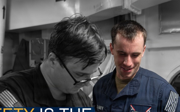 A U.S. Navy promotional safety poster featuring two sailors reviewing documents together in what appears to be a shipboard interior. The image uses selective color, with one sailor in full color wearing a blue Navy uniform with a name tag reading 'Austin Dockins,' while the background and other sailor are rendered in black and white. The overlay text reads 'SAFETY IS THE #1 PRIORITY.'