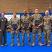 Seven military personnel pose for a group photo in what appears to be a gymnasium or indoor facility. Three individuals in the center are holding plaques or awards featuring what appears to be the Arizona state symbol in blue and gold. A banner in the background references the '944th Fighter Wing,' indicating this is a U.S. Air Force Reserve unit award ceremony.