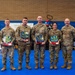 Seven U.S. Air Force personnel in OCP (Operational Camouflage Pattern) uniforms pose for a group photo at what appears to be an awards ceremony. Four of the individuals are holding decorative plaques featuring what appears to be the Arizona state flag design in blue, gold, and red. The event appears to be associated with the 944th Fighter Wing based on a visible banner in the background.