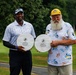 Two men are posing outdoors on a golf course, each holding a circular wooden award plaque. The plaques are from the 2026 Medal of Honor Base Championship — one for Men's Division 1st Place Net and the other for Senior Division 1st Place Net. Both men are smiling, dressed in golf attire, with a lush green course visible in the background.