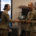 Two U.S. Air Force personnel in OCP (Operational Camouflage Pattern) uniforms are shaking hands in what appears to be an office setting. The male service member on the right has 'U.S. AIR FORCE' tape visible on his uniform and appears to be of senior rank. The interaction appears to be a formal recognition or greeting ceremony.