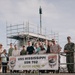A group of approximately 15 people, including uniformed U.S. Navy personnel and civilians, pose for a photo in front of a banner reading 'USS Mississippi SSN 782 - Gator Done.' The setting appears to be a naval facility or pier, with scaffolding and what appears to be a submarine sail structure visible in the background. The phrase 'Gator Done' suggests the completion of a maintenance period or availability period.